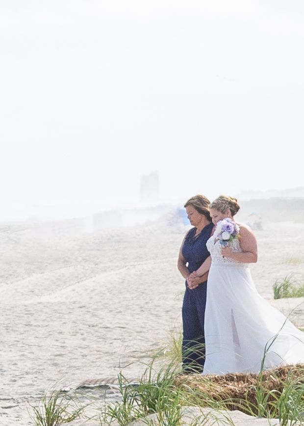 A bride being walked down the aisle on a misty beach with grasses in the foreground during a wedding ceremony.