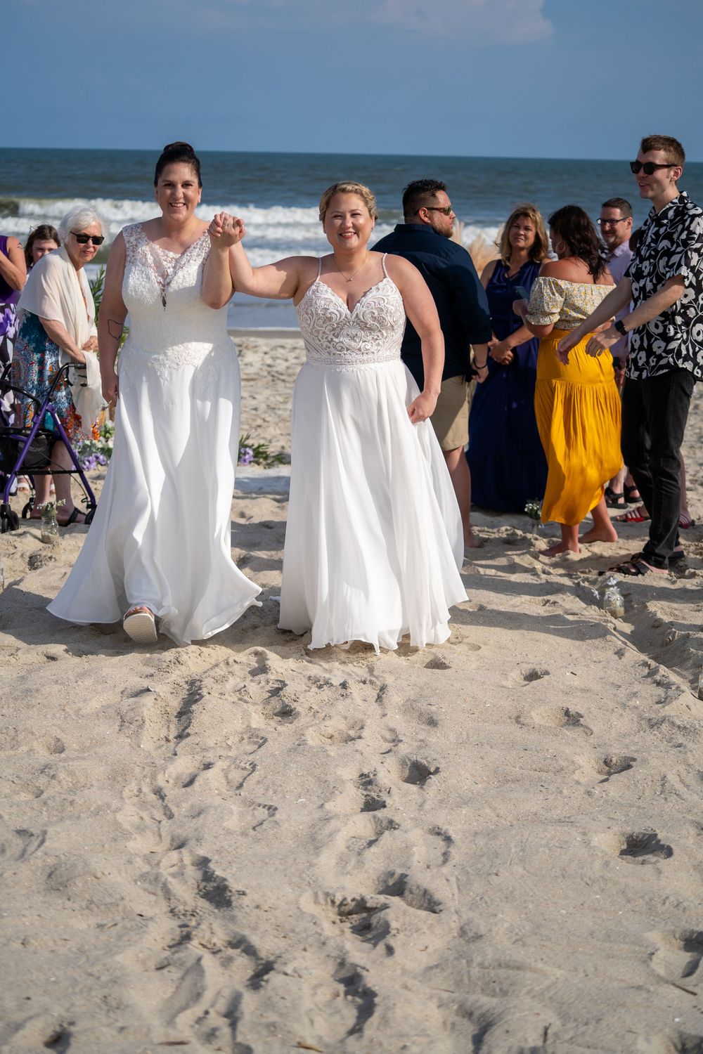 beach wedding photo showing people in white dresses walking down the aisle together on sandy shores by the ocean.