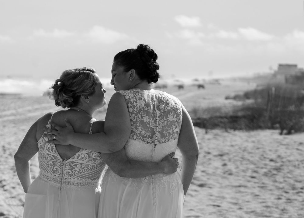 Black and white wedding couple embraces on a beach with ocean waves in the background.