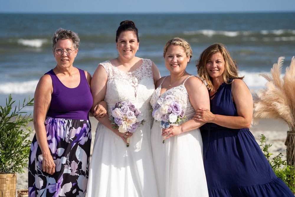 Wedding party in navy blue and purple dresses gathered at the beach for wedding day photos.