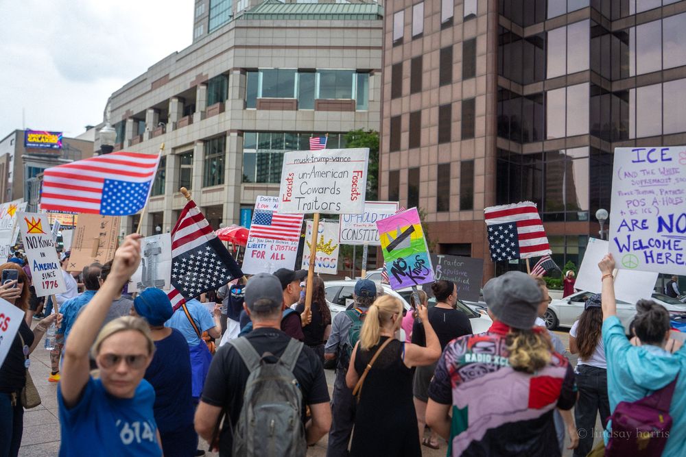 Protesters gather outside a federal building holding American flags and signs during a political demonstration.