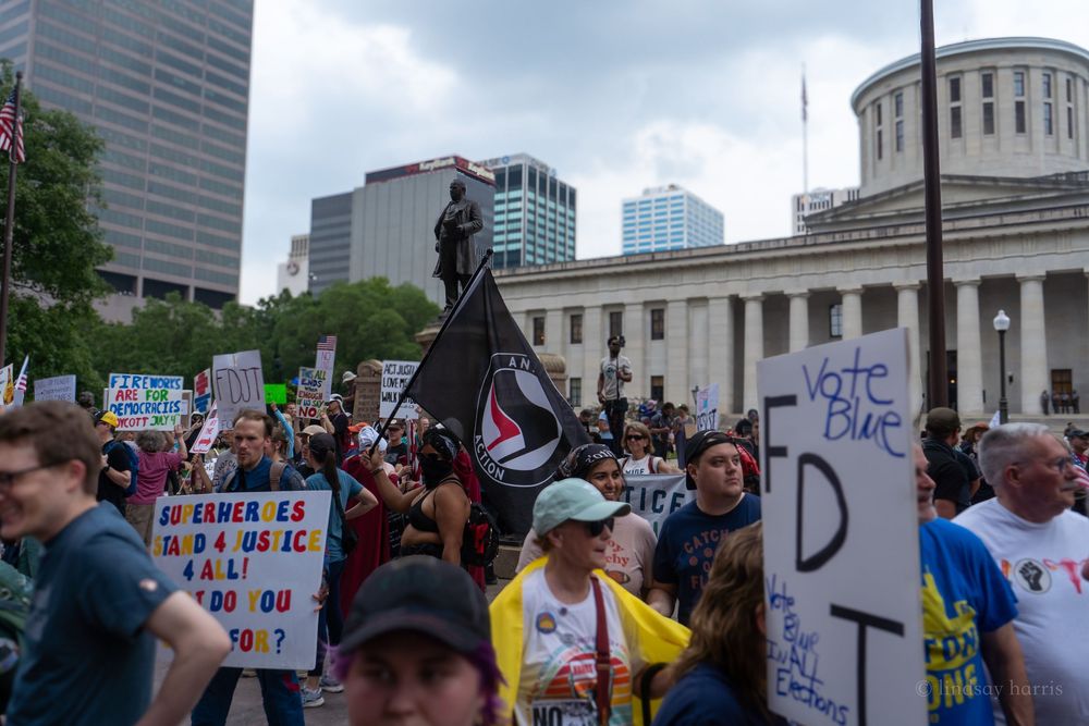 Protesters gather outside a government building holding signs during a demonstration on a cloudy day.