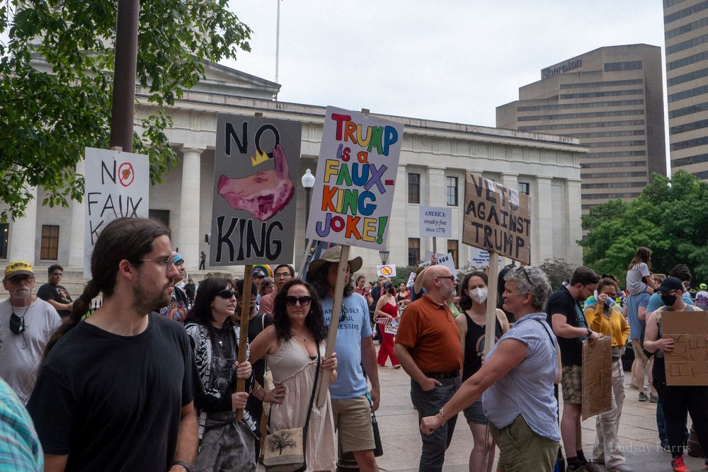 Large crowd of protesters gathering on city street with protest signs and banners during a demonstration march.