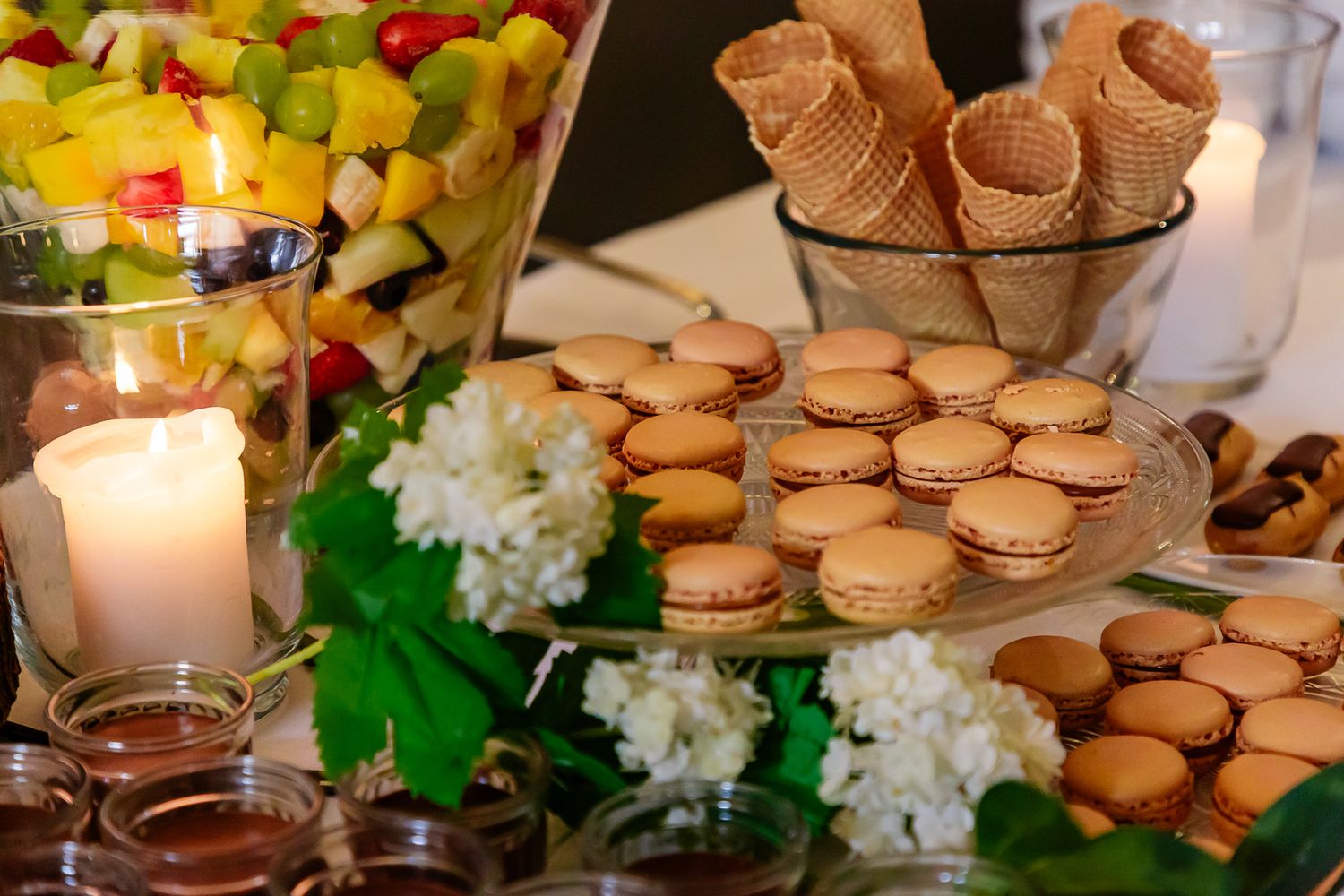 Tiered display of French macarons arranged on elegant dessert stands with floral decor and candlelight.