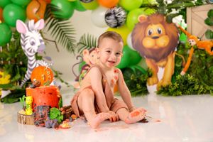 Jungle themed cake smash setup with green foliage, balloons and safari animal decorations.