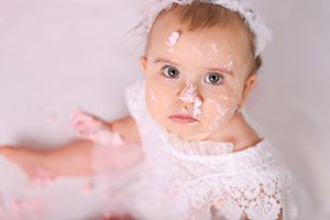 Close up of baby covered in cake frosting wearing white lace outfit.