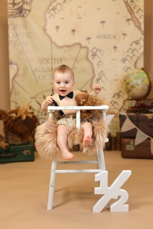 Baby sitting in high chair with adventure themed backdrop featuring world map and globe.