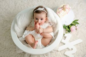 A baby in white lace outfit rests in a vintage porcelain wash basin surrounded by delicate floral accents.