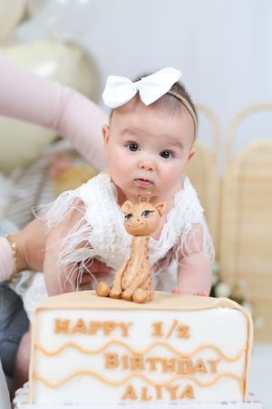 First birthday cake with teddy bear decoration and white bow accents.