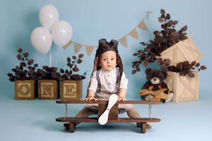 Rustic first birthday setup with wooden shelf, white balloons and bunting against blue wall.