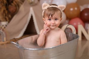 Baby takes a bubble bath in rustic wooden tub during milestone photo session.