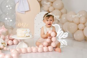 Elegant pink and white balloon garland backdrop with cake smash setup.