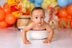 Vibrant orange and blue balloon backdrop with white bathtub prop for cake smash session.