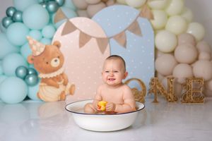 Whimsical cake smash set with teal and cream balloons, teddy bear decor, and bathtub prop.