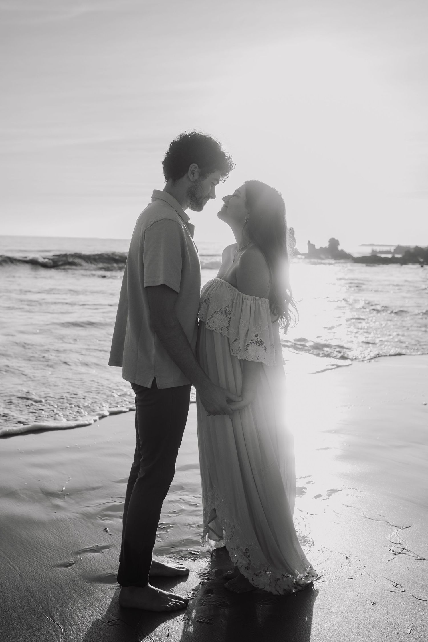 Black and white beach photo series of couple in romantic poses by the ocean.