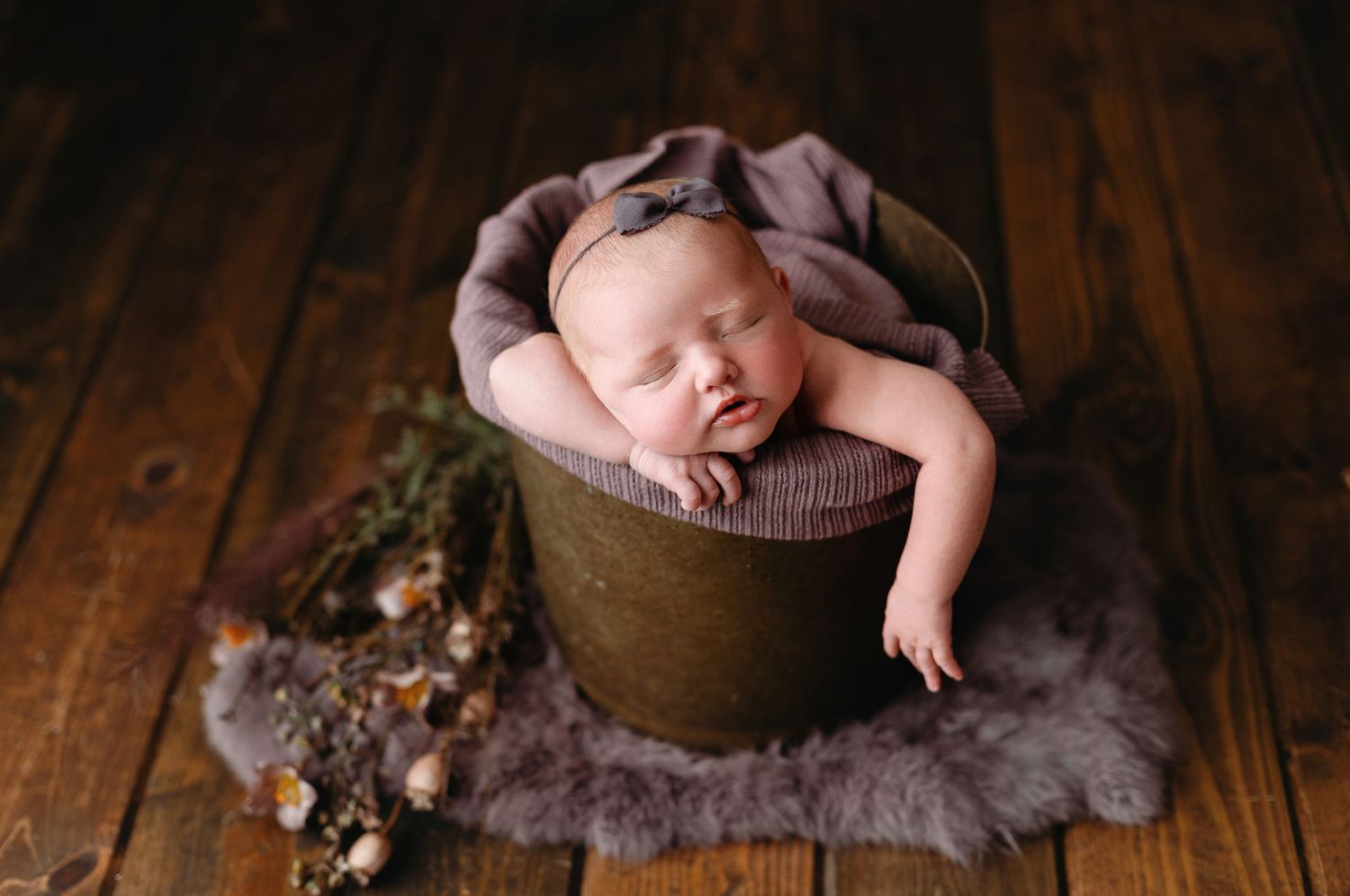 A baby girl in a bucket with one arm out with purple accents.  - Greenville SC newborn photographer - Easley SC newborn photographer