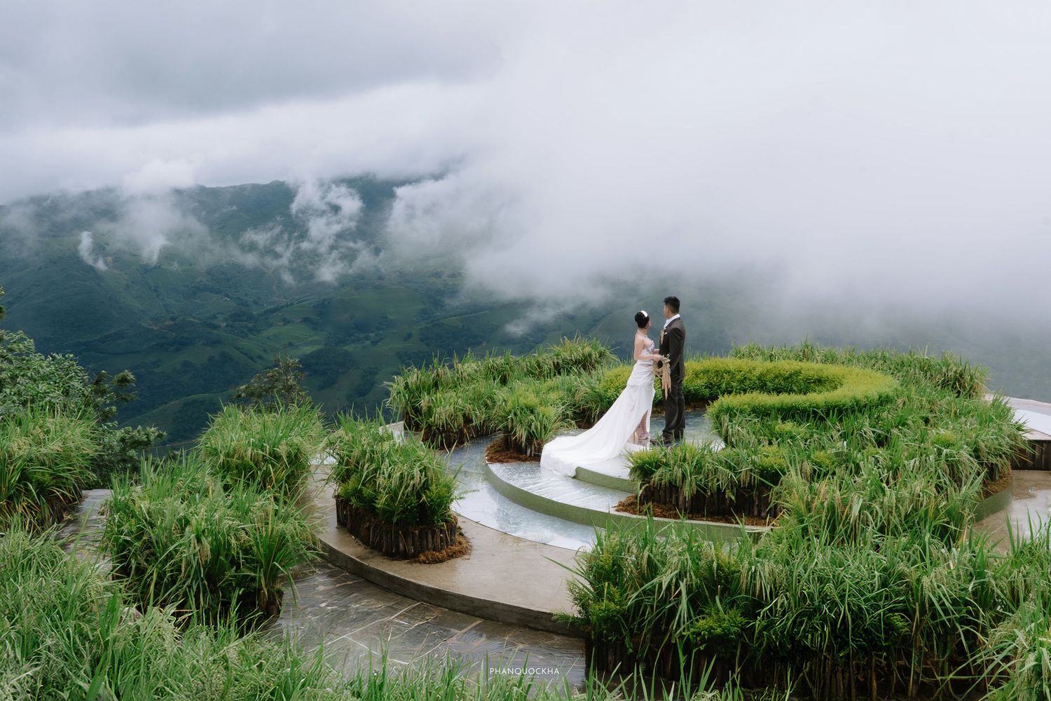 Bride and groom standing in spiral rice terrace garden surrounded by misty mountain landscape.