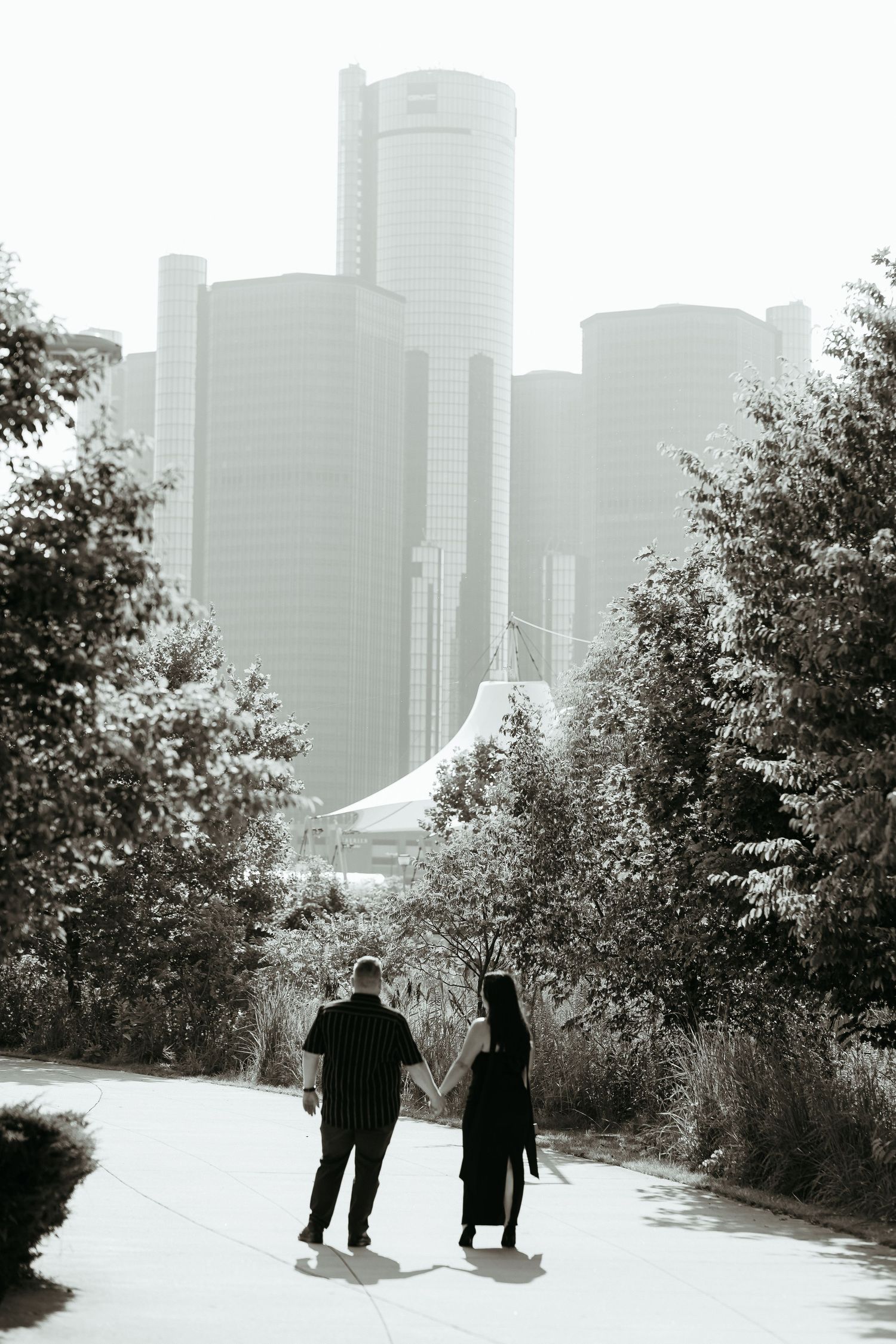 A couple holding hands while walking with Detroit's Renaissance Center skyline in the background. Engagement session.