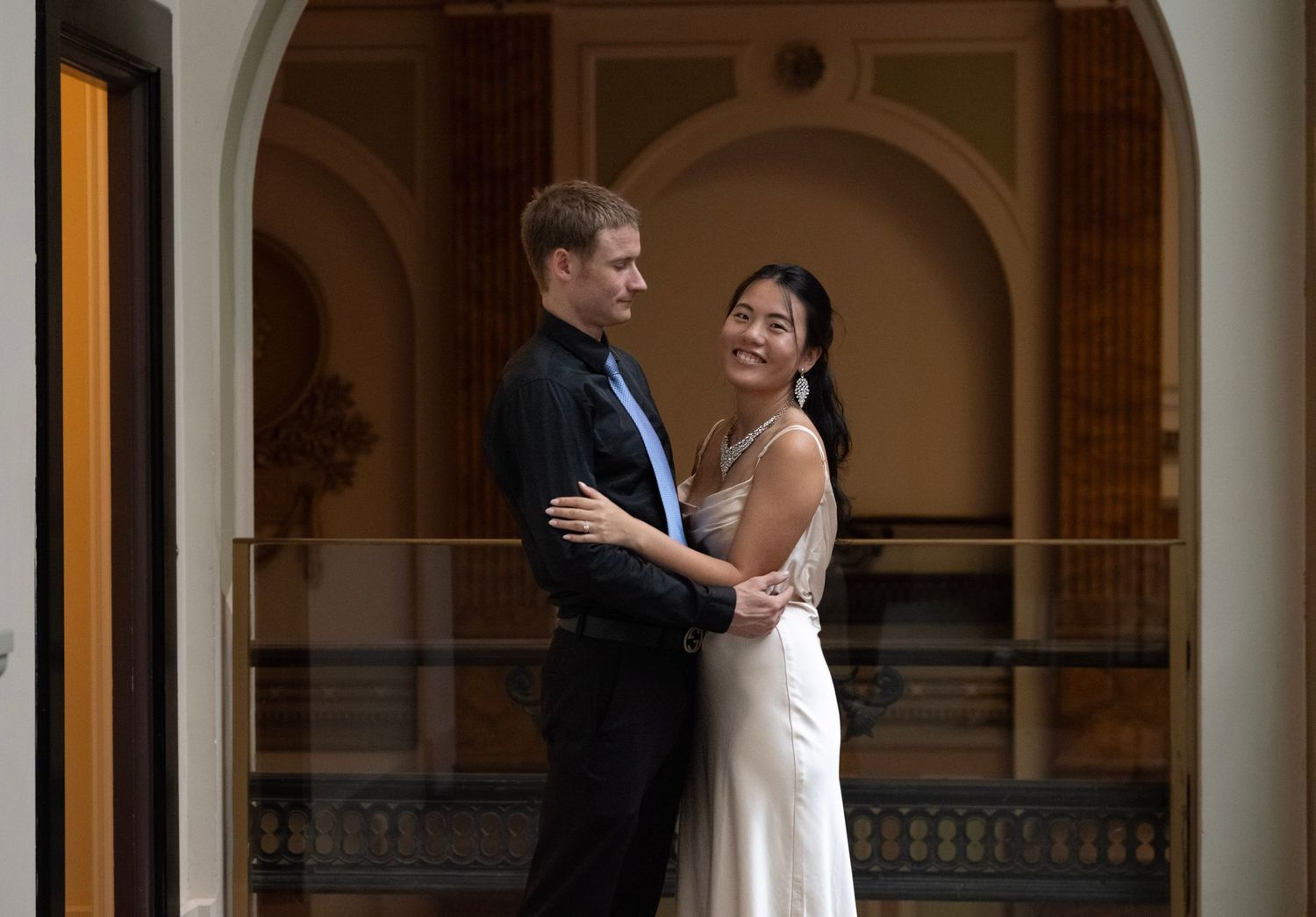 A couple shares a romantic dance moment under an elegant arched colonnade.