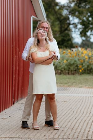 Playful engagement photos taken in front of a red barn with rustic wooden planks. Timeless love stories and true to color photography