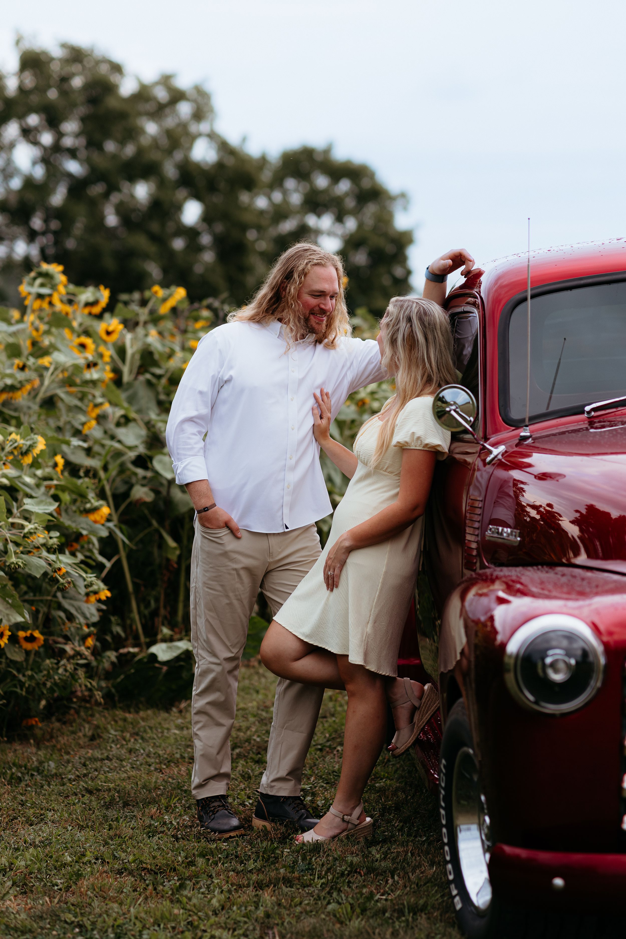 Romantic couple poses by vintage red truck in a sunflower field.
