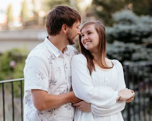Couple in white outfits sharing intimate moment outdoors during sunset.