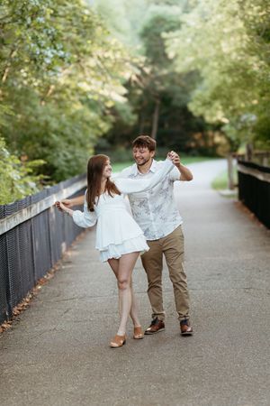 Couple dancing and laughing on tree-lined path in Rockford Michigan. Playful candid documentary engagement session. Fun and free couples.