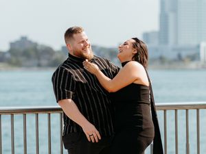 Joyful couple laughing together on waterfront deck with Detroit city skyline in background.