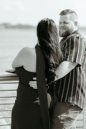 Black and white romantic engagement photos showing a couple embracing by a railing. Detroit Waterfront engagement session. Timeless photos.