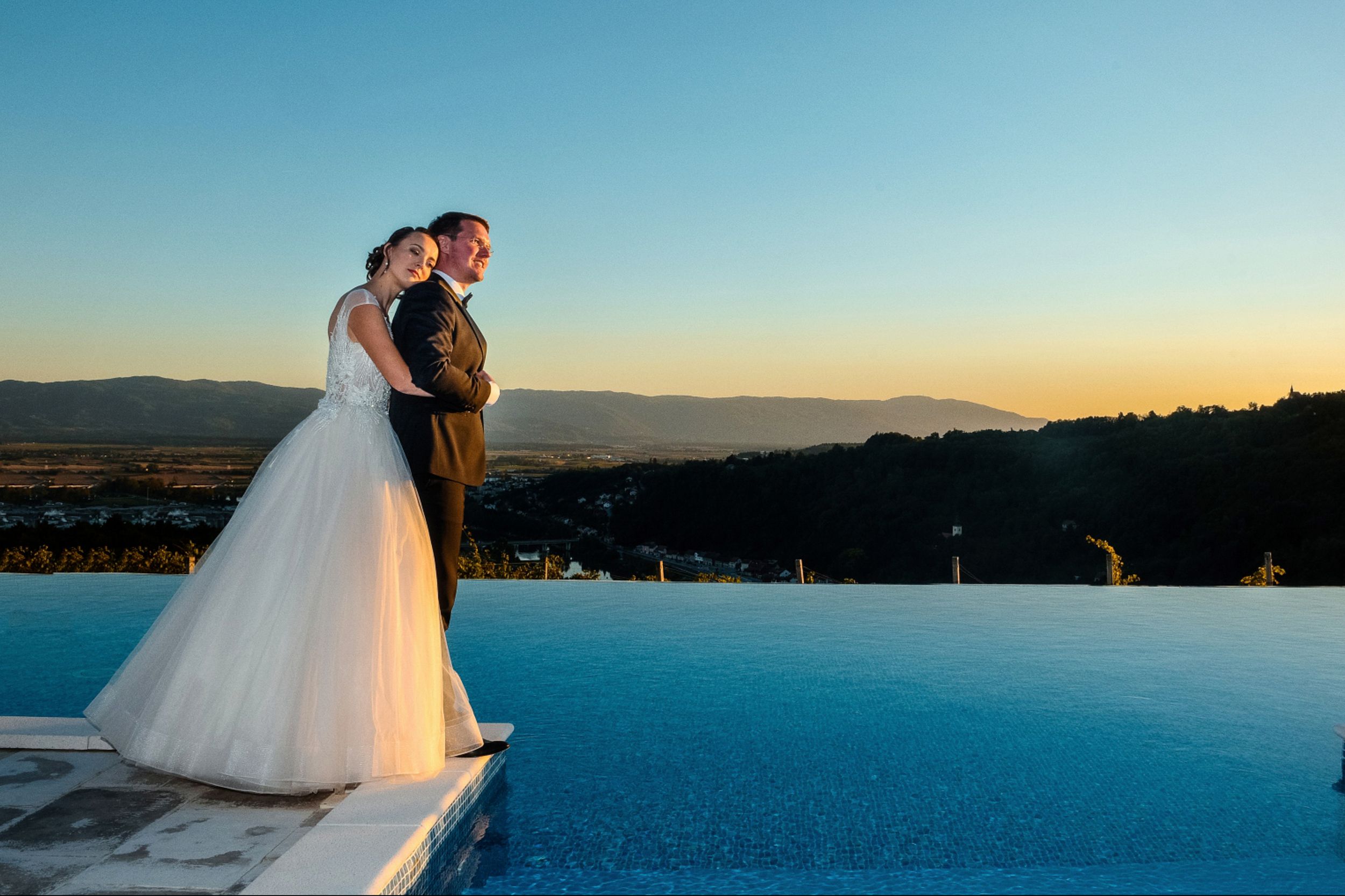 Elegant wedding couple silhouetted against blue sky and mountain backdrop. Restavracija Tri Lučke, Krško