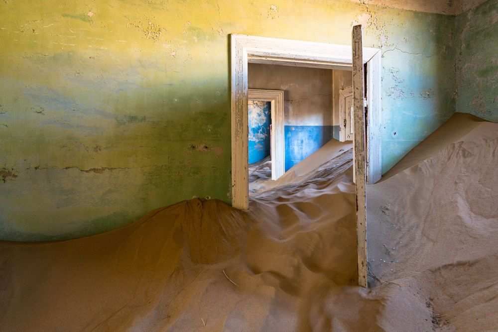 Interior room of an abandoned building filled with sand dunes stretching from floor to ceiling.