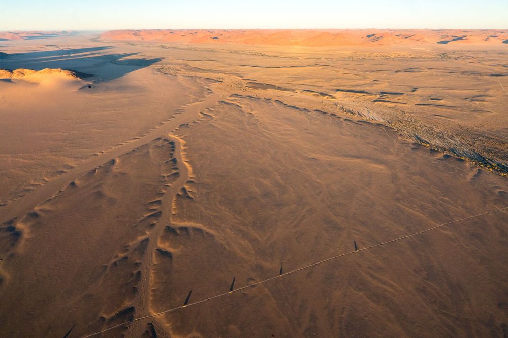 Aerial footage showcases expansive desert landscape with winding canyons and ridges sculpted by erosion in warm sunlight.