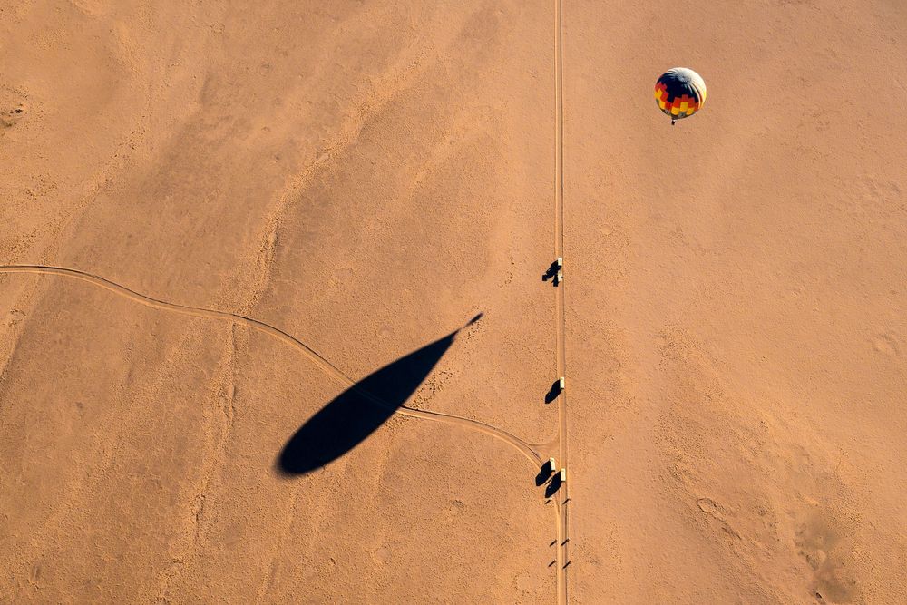 Aerial view of dark shadow cast by a hot air balloon gliding over golden desert sand dunes in a picturesque setting.