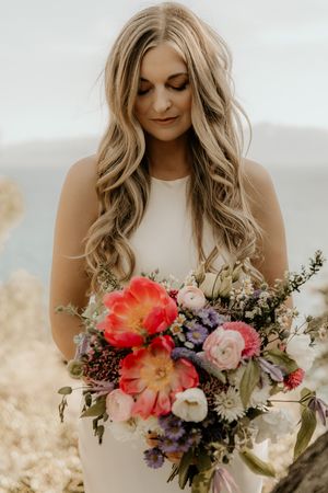 Close-up series of someone in a white dress holding a vibrant bouquet of pink, red, purple and white flowers in natural light.