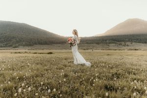 A couple stands in a scenic mountain meadow at sunset with wildflowers surrounding them in the Colorado wilderness.