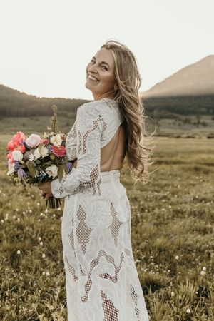 Whimsical bridal portraits in a golden meadow at sunset featuring a lace dress and vibrant pink bouquet.