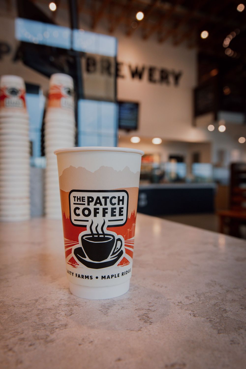 Coffee shop logo and branding elements shown on takeout cups with blurred cafe interior background.