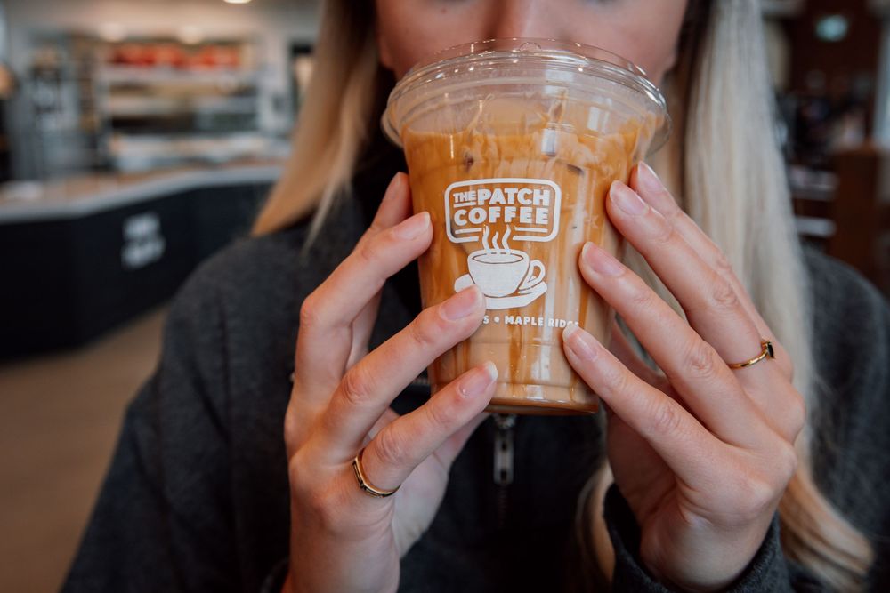 Person holding clear plastic cup of iced coffee beverage with Coffee NW logo in front of blurred cafe background.