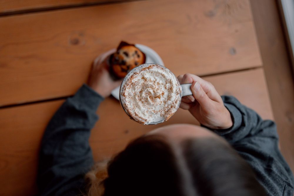 Series of hands holding up small cups of espresso coffee drinks in a warm wooden setting.