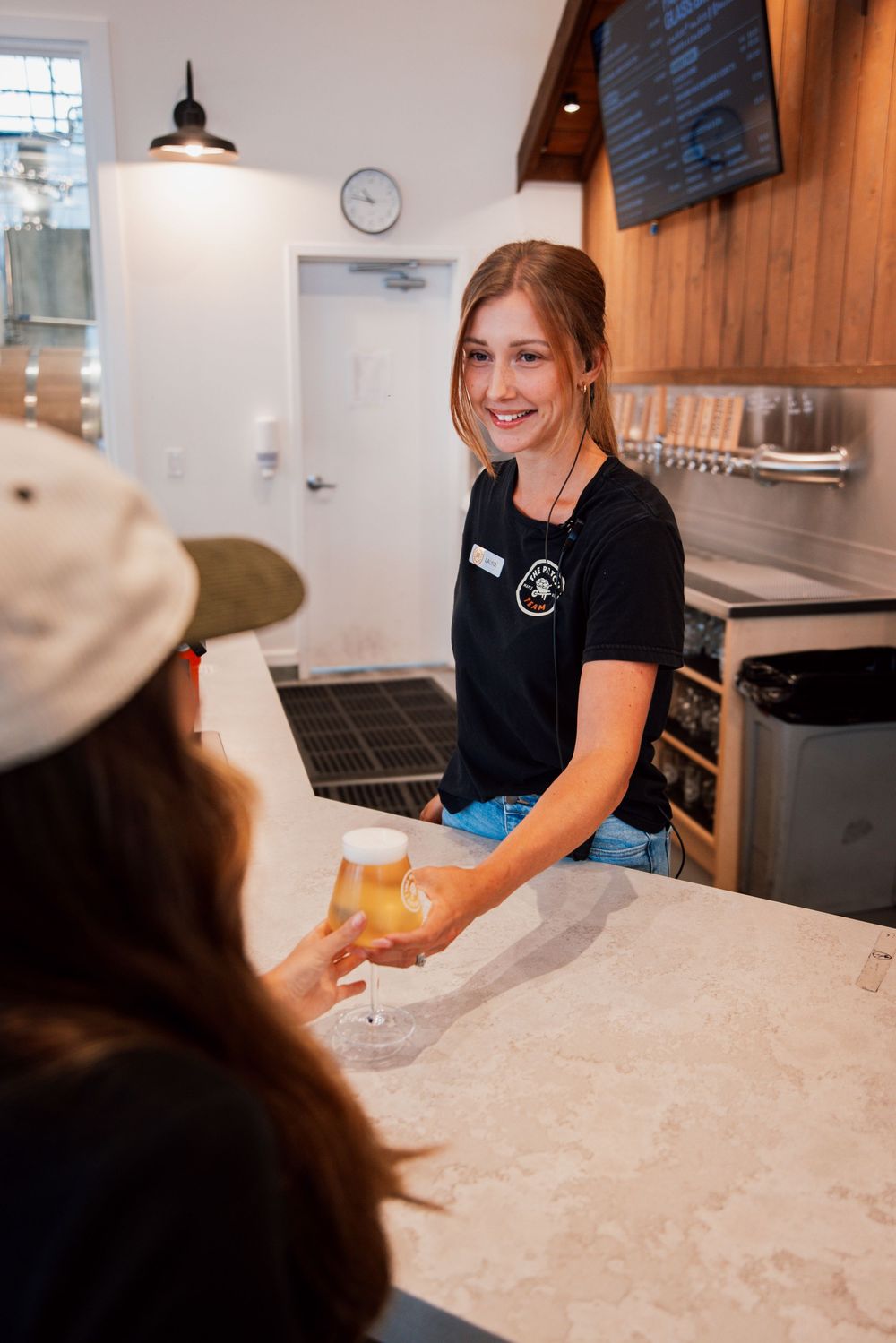 Staff member serving a craft beer at a bar counter with wooden decor and white walls in the background.
