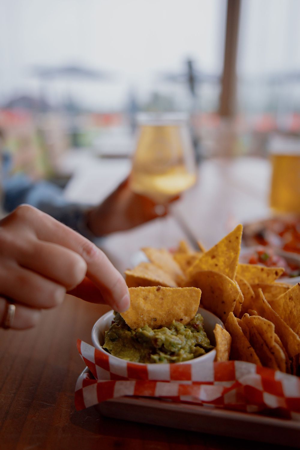 Close-up shot of hands reaching for tortilla chips with fresh guacamole dip served in a casual restaurant setting.