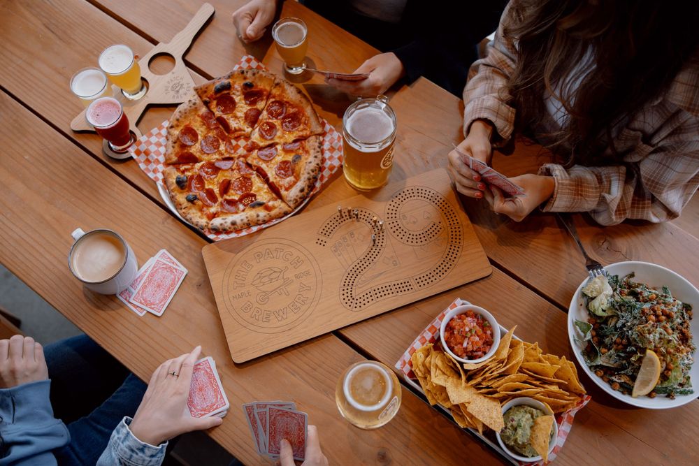 Aerial view of friends sharing pizza, french fries and salad at wooden table with drinks and playing cards.