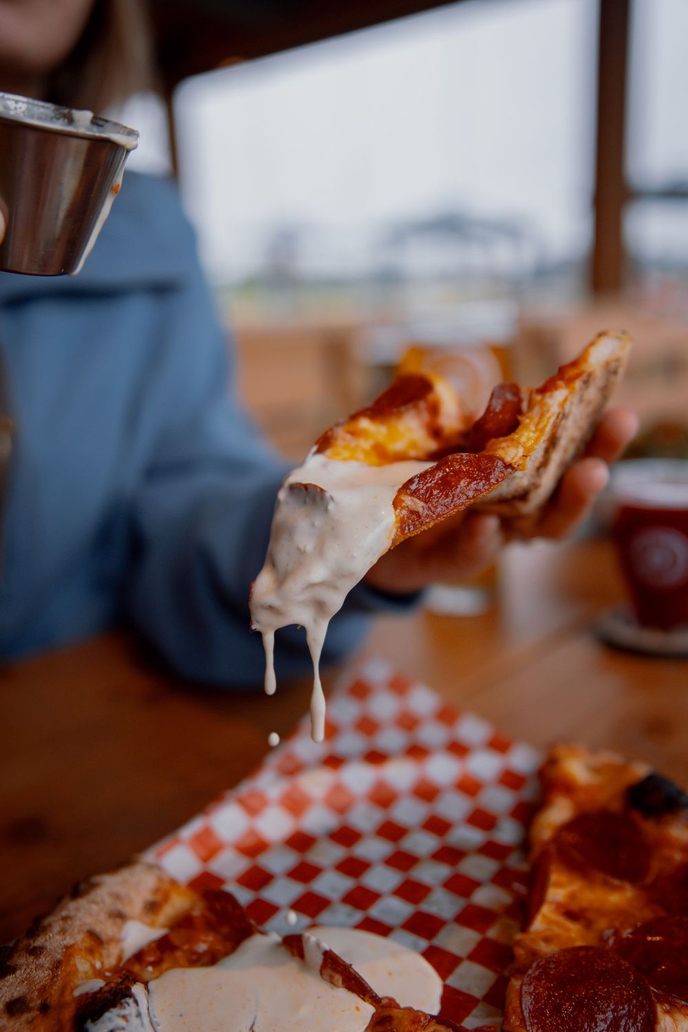 Stretchy melted cheese pulls away from a slice of pizza topped with pepperoni on a red and white checkered surface.