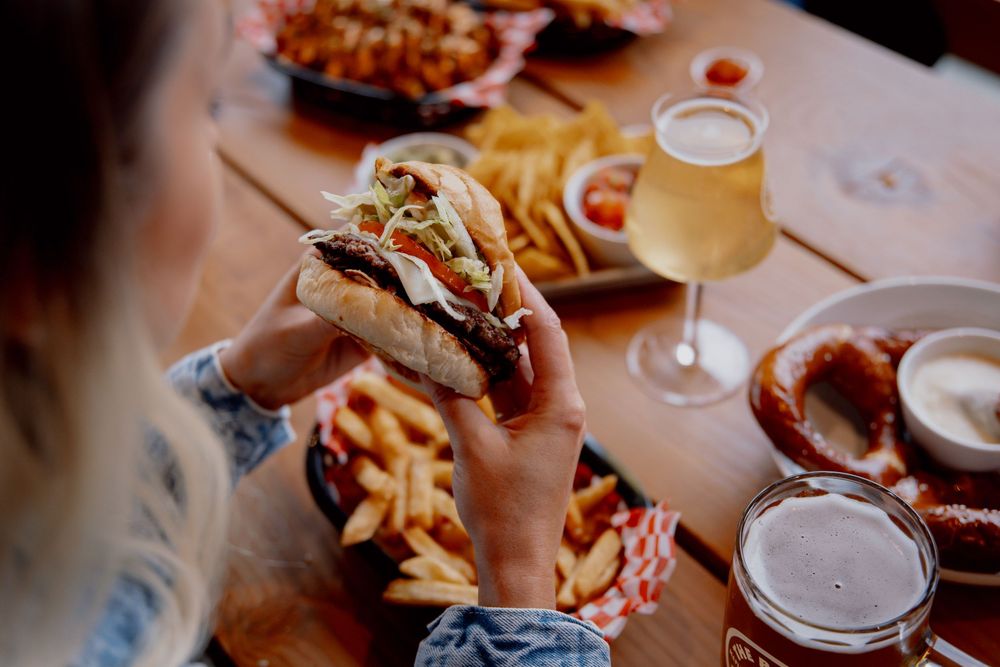 Beer glasses and bar food including french fries, sandwiches and appetizers spread across a wooden restaurant table.