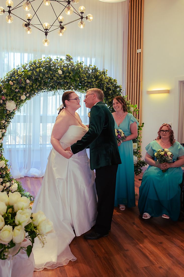Four sequential photos showing a couple sharing their first kiss as newlyweds under a floral arch during a wedding ceremony.