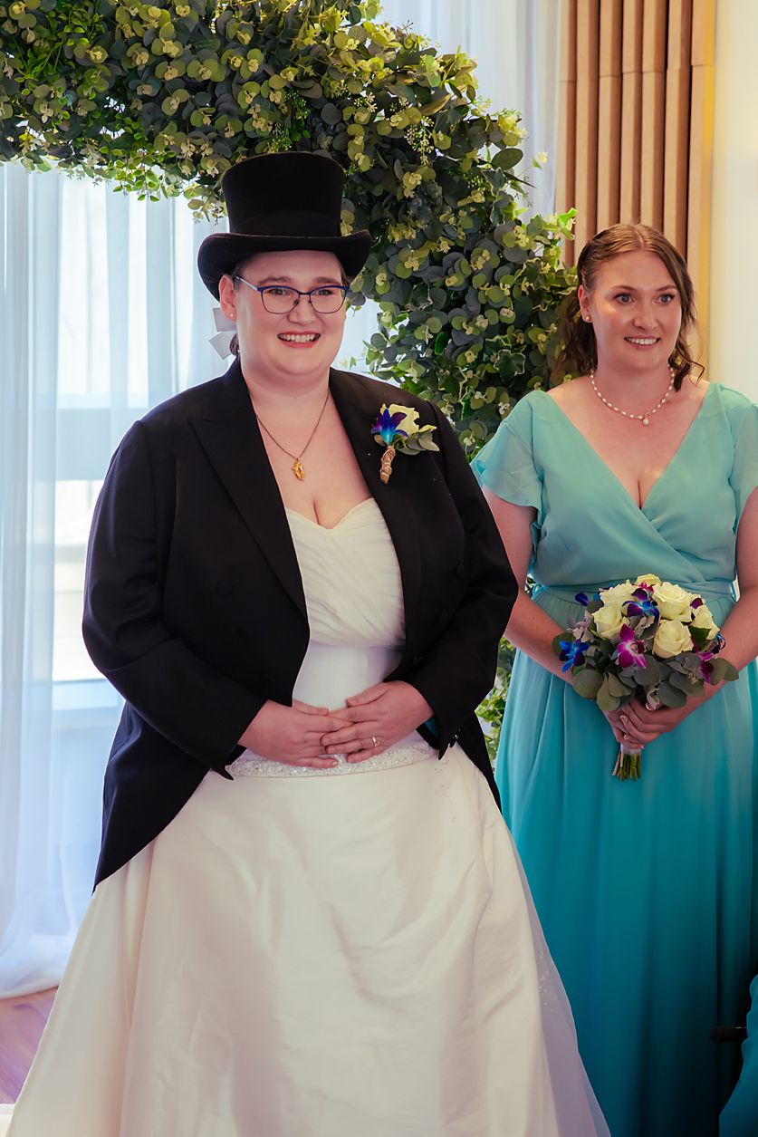 Wedding party members wearing teal bridesmaid dresses and black shawls stand next to someone in a white wedding dress.