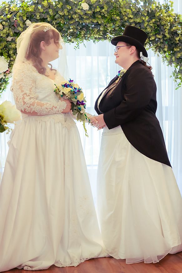 A couple shares their first dance at a wedding reception under decorative floral arches and white drapery.