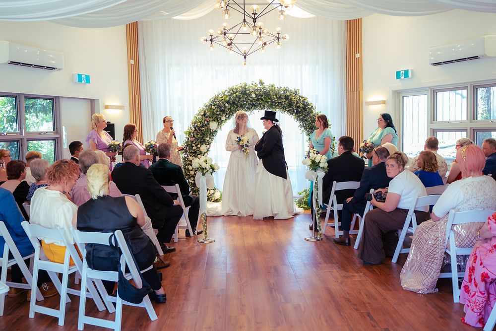 Panoramic view of an elegant wedding ceremony setup in a bright white indoor venue with guests seated in rows.