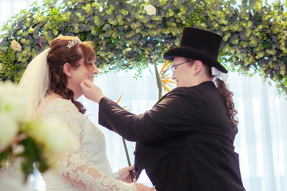 A romantic outdoor wedding ceremony features a couple embracing under a lush green canopy of trees and flowers.