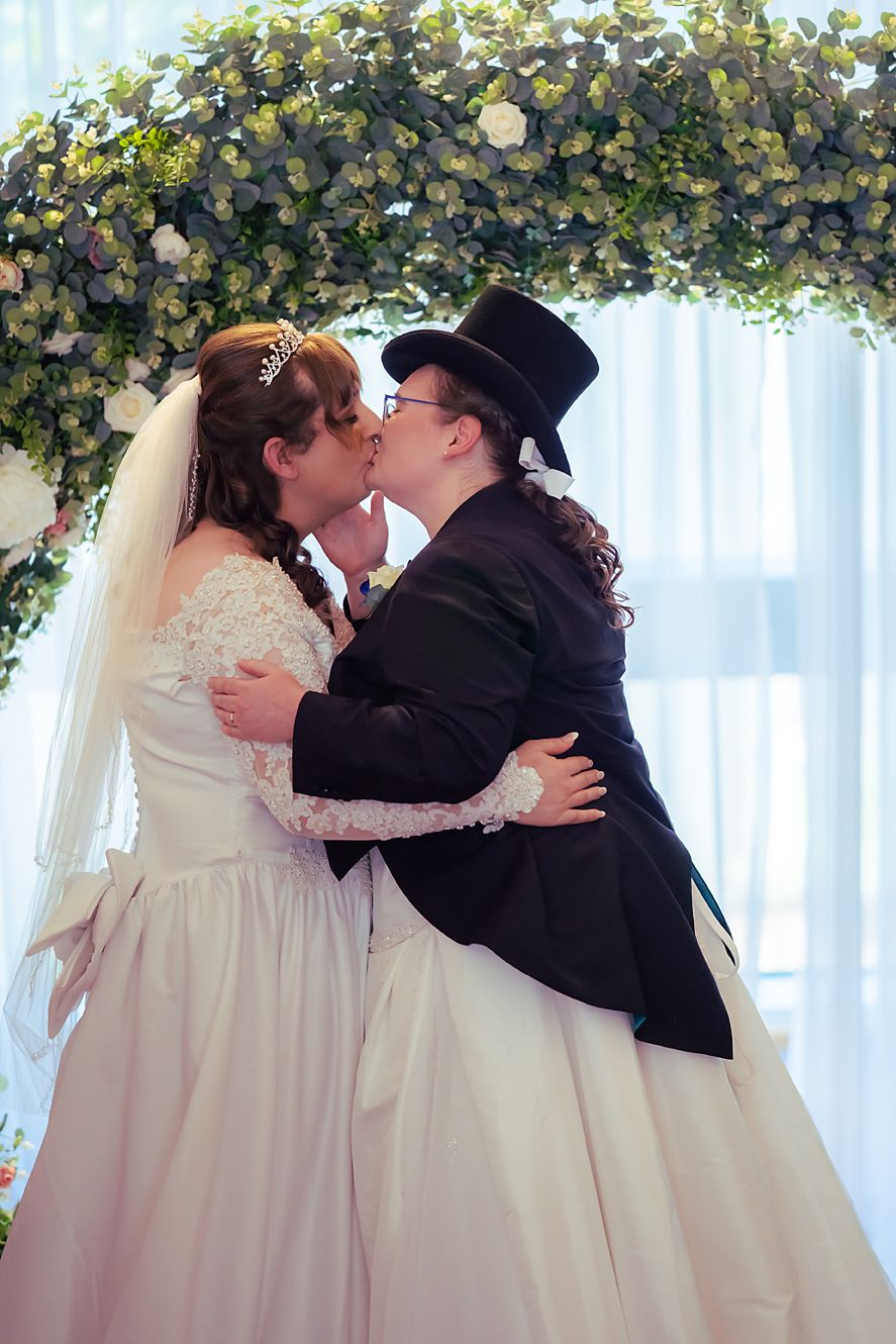 Romantic sequence of wedding couple sharing their first kiss as newlyweds under a floral archway.